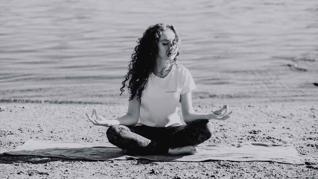 A woman meditating on the beach with her legs crossed and eyes closed, finding calm and balance near the water.